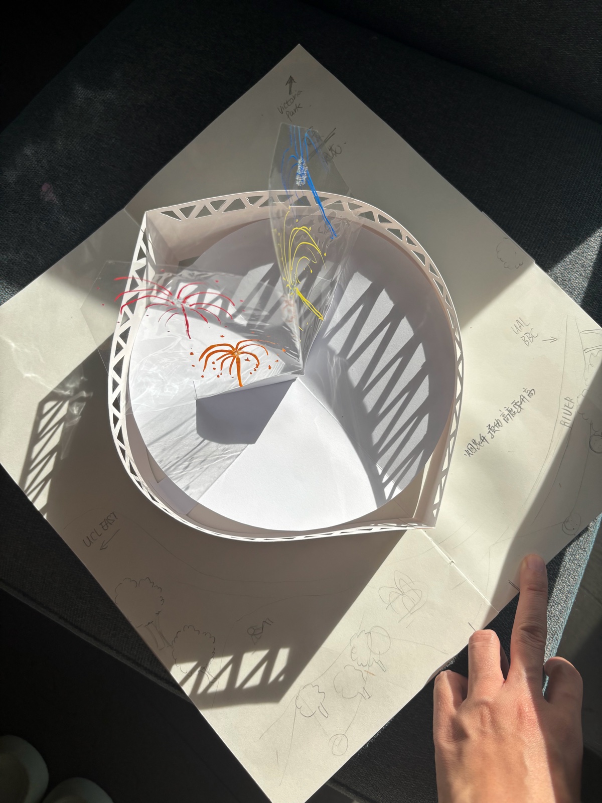 Here is East Bank — a white paper pop-up model with a curved, lattice-cut tower, photographed in the sun