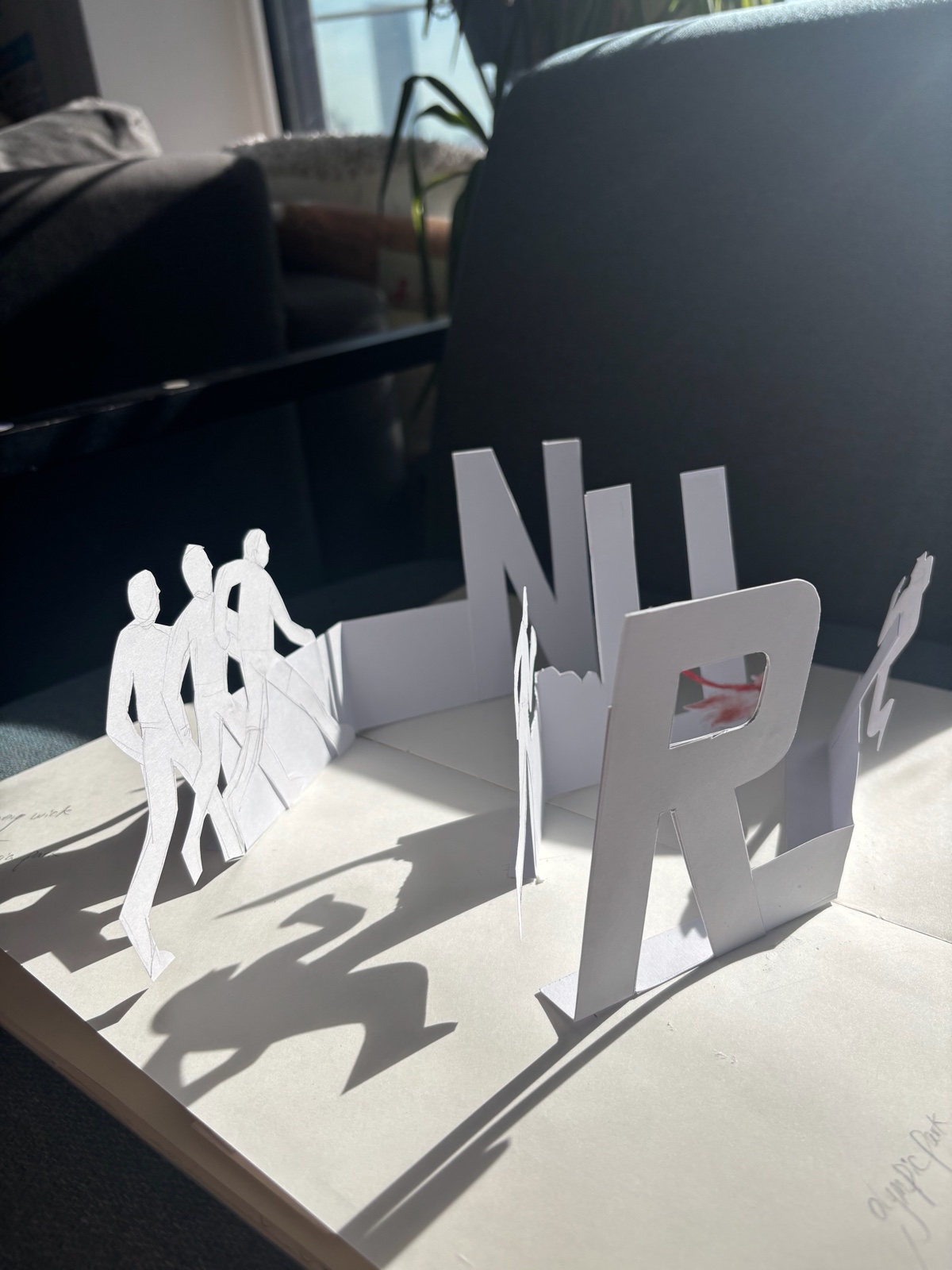 Here is East Bank — cut-paper figures and large letters standing on a paper model, casting shadows