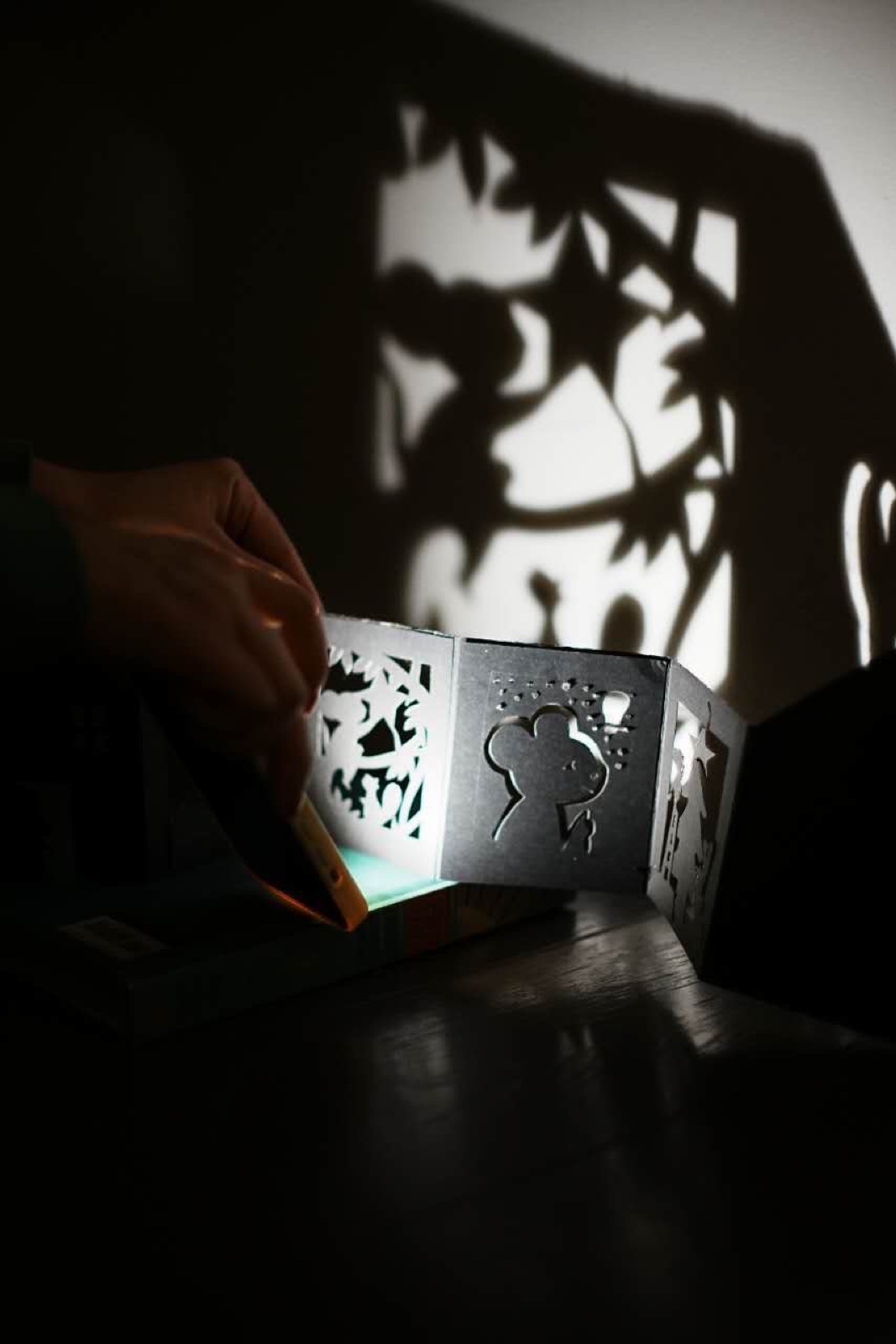 A workshop: a hand folding a paper lantern so the light shines through the cut-out shapes