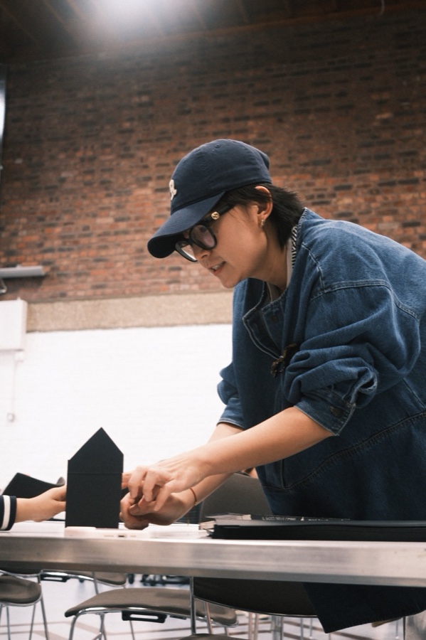 The artist in a cap at a table, folding paper during a pop-up book workshop
